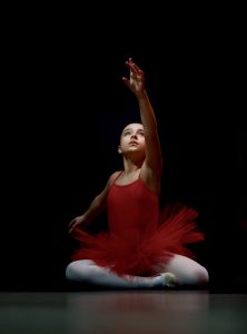 Ballerina in red tutu elegantly poses under spotlight, highlighting graceful movement.