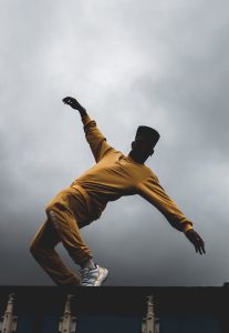 A dancer in vibrant yellow attire executes a dynamic pose against a dramatic cloudy sky, captured in a low angle shot.