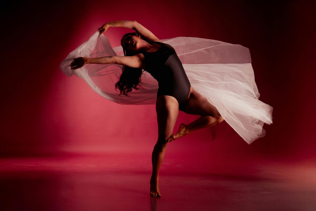 Elegant Latina dancer performing in a studio with white scarf and red backdrop. Captivating graceful movement.